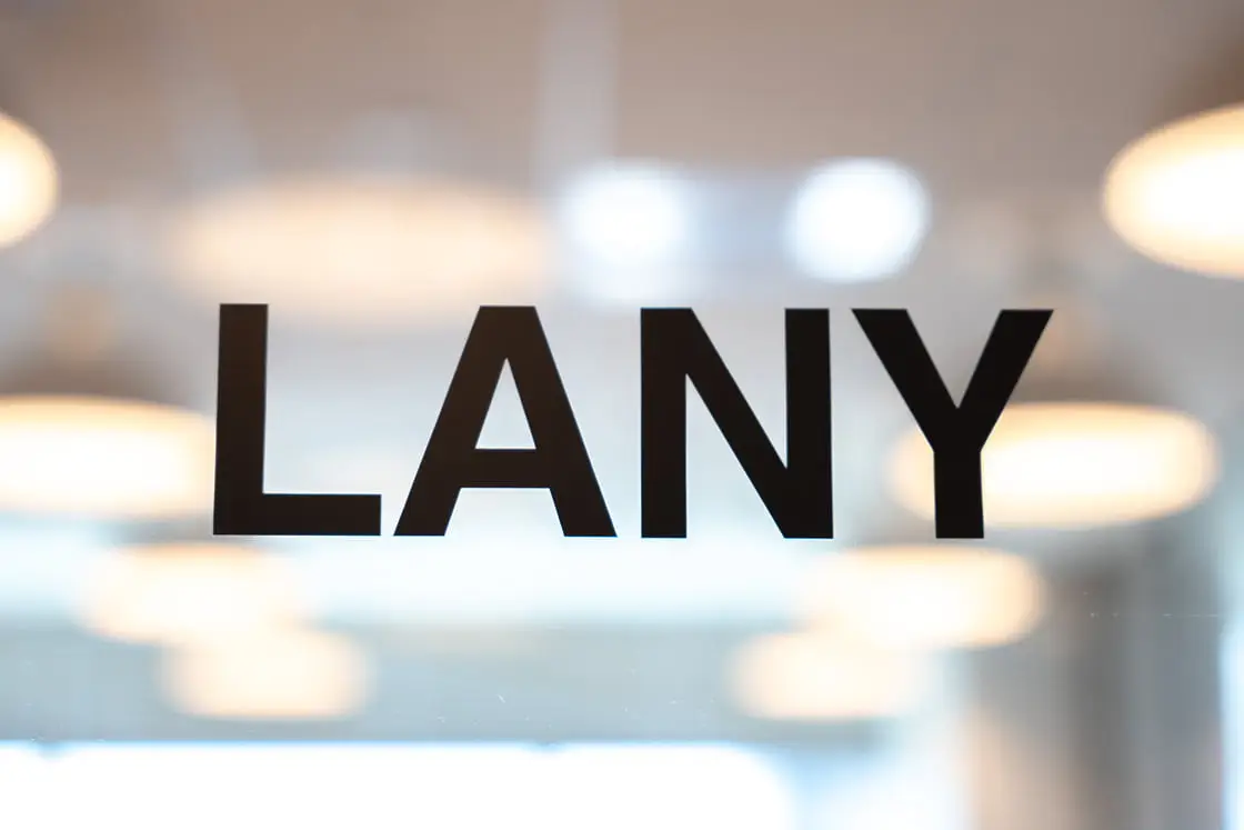 ガラス越しに見える「LANY」の黒いロゴと、ぼんやりと光るオフィス照明の背景を捉えた写真