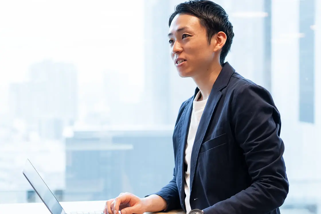オフィスでノートパソコンに向かいながら話すビジネスパーソン