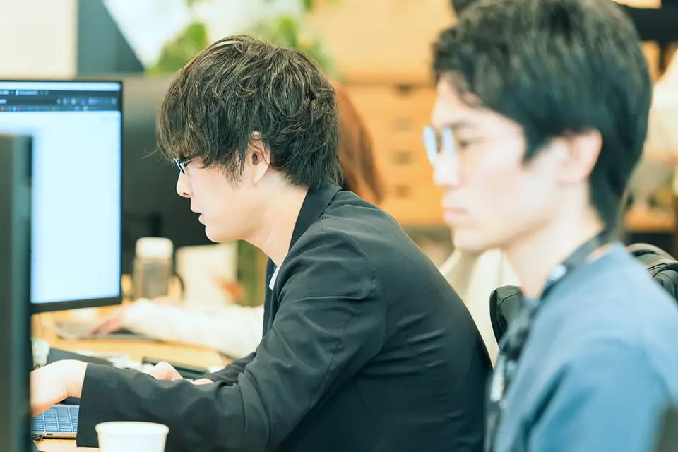 パソコンに向かって真剣に作業する男性たちが並ぶオフィスの風景